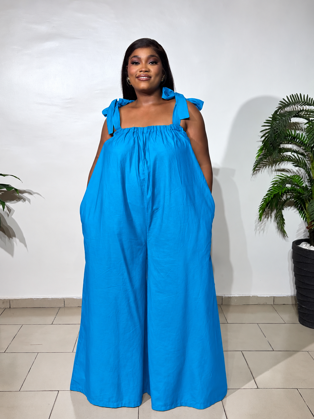 Solara jumpsuit with a gathered neckline, statement shoulder ties, and flowy wide-leg trousers, styled for effortless elegance.