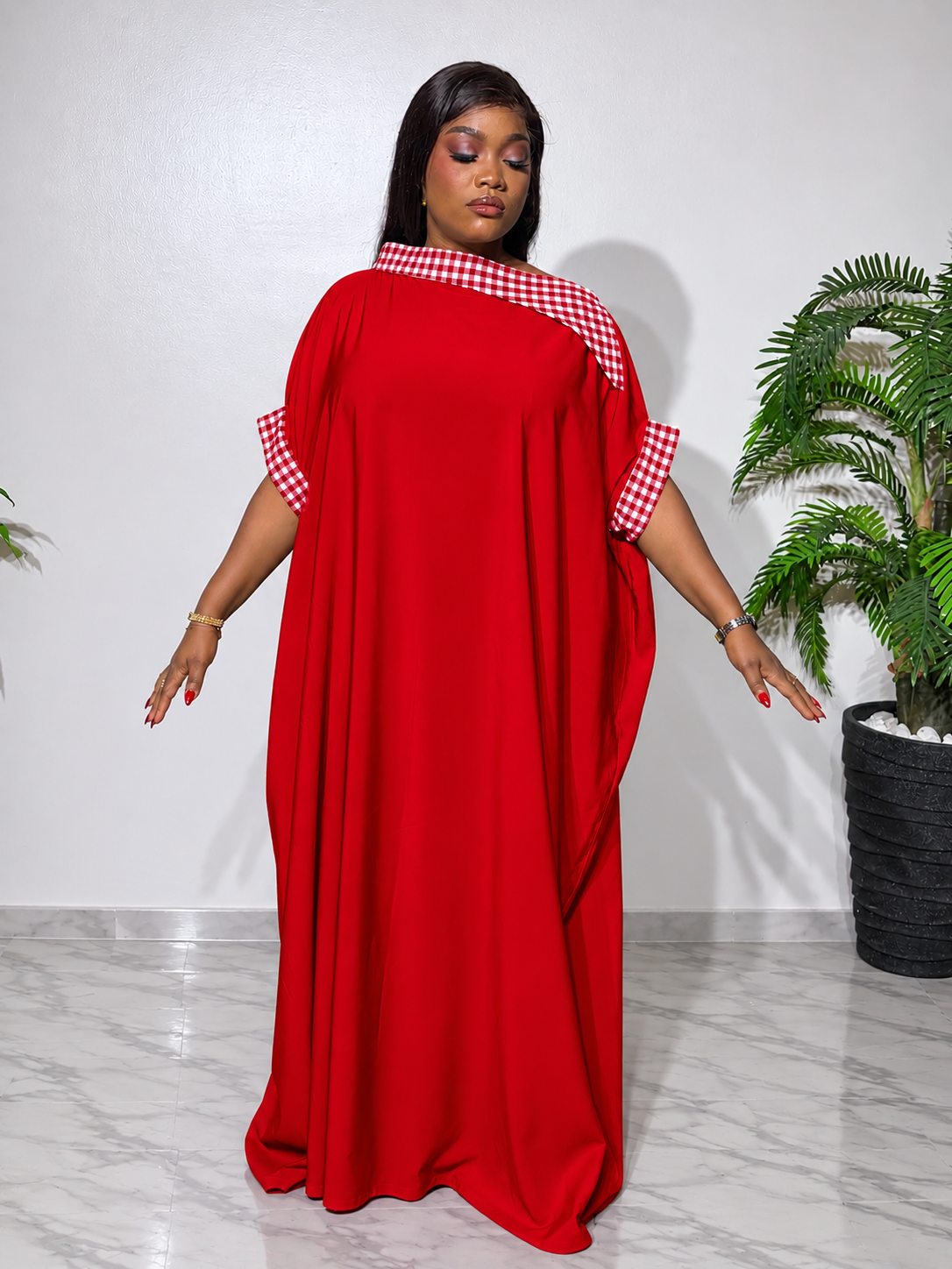 Elegant red boubou with red-and-white checkered accents, featuring a flowing silhouette, statement cape sleeves, and a luxurious finish.